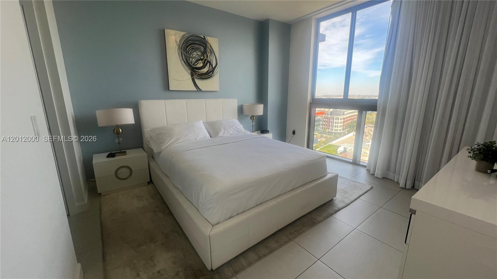 A modern bedroom features a white bed, blue accent wall, and floor-to-ceiling windows — 5350 NW 84th Ave # 1605, Doral FL 33166, DORAL, FL