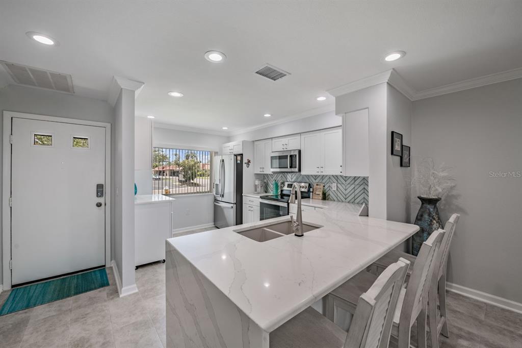 A modern kitchen features white cabinets, a marble-topped island with seating, and stainless steel appliances — 19029 US HIGHWAY 19 N UNIT 27A, CLEARWATER, FL