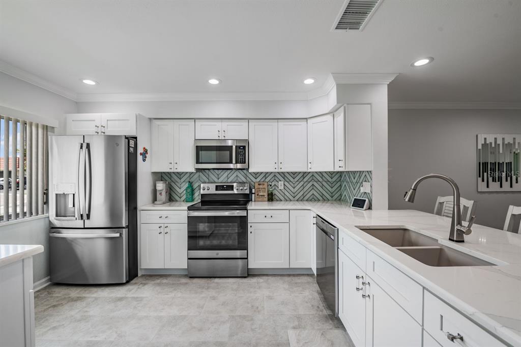 A modern kitchen features white cabinets, stainless steel appliances, a herringbone backsplash, and quartz countertops — 19029 US HIGHWAY 19 N UNIT 27A, CLEARWATER, FL