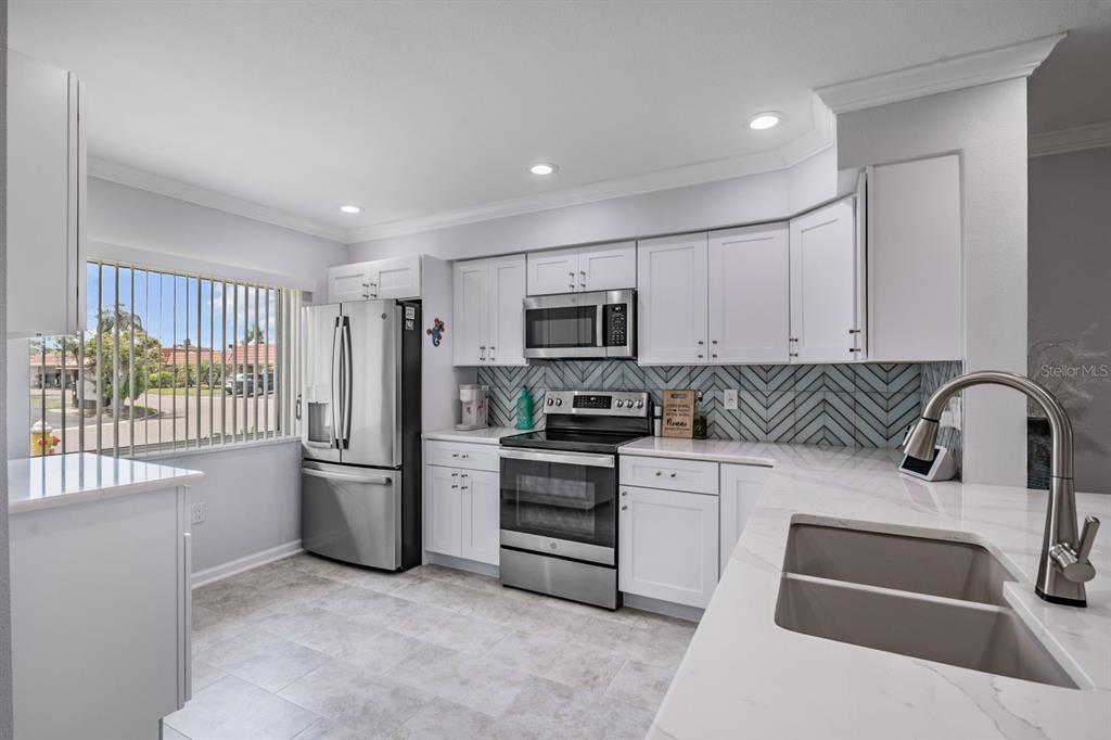 A modern kitchen features white cabinets, stainless steel appliances, a herringbone backsplash, and quartz countertops — 19029 US HIGHWAY 19 N UNIT 27A, CLEARWATER, FL