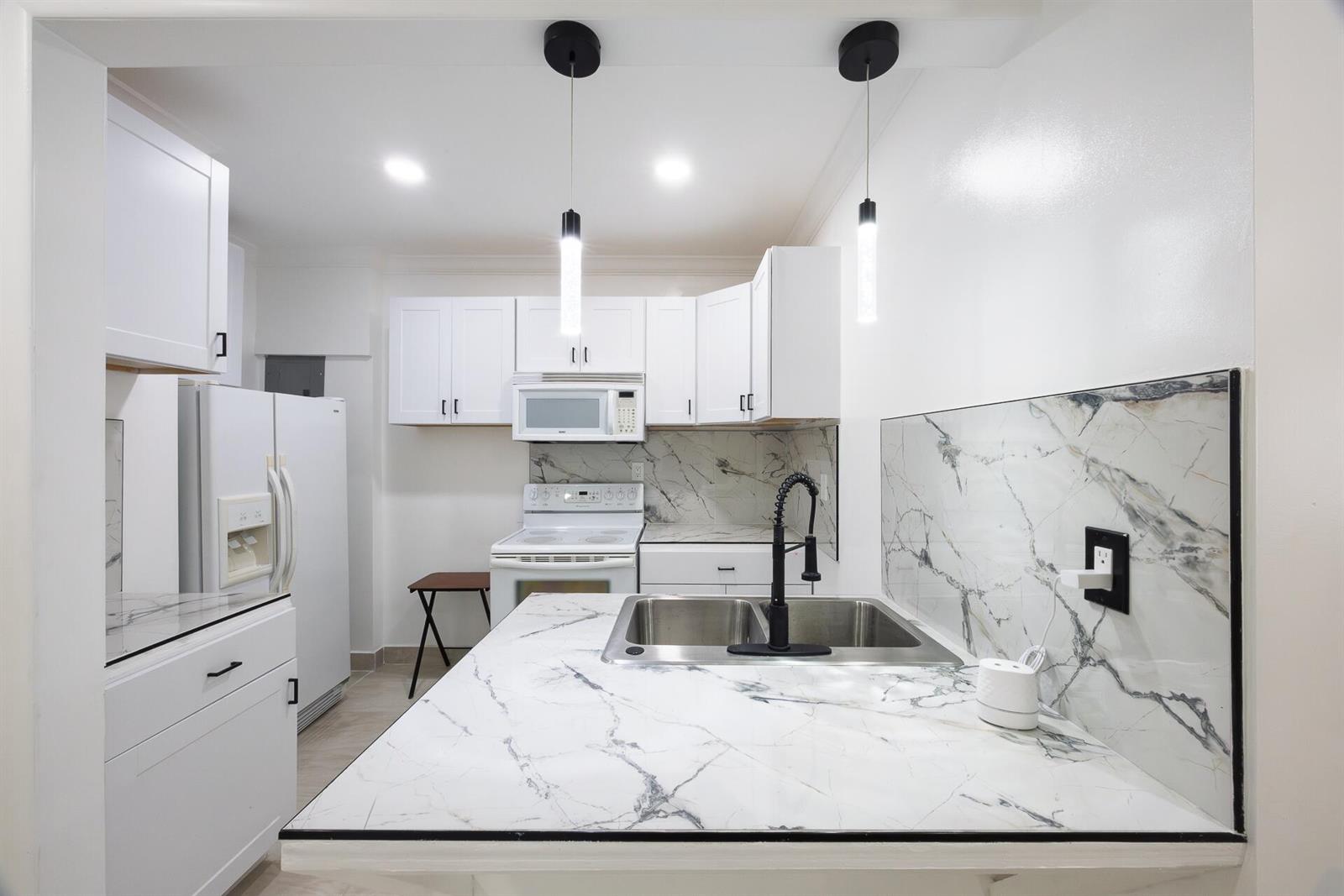 A kitchen features white cabinets, marble-patterned countertops and backsplash, and a stainless steel sink — 4591 Purdy Lane # 1, West Palm Beach FL 33415, WEST PALM BEACH, FL