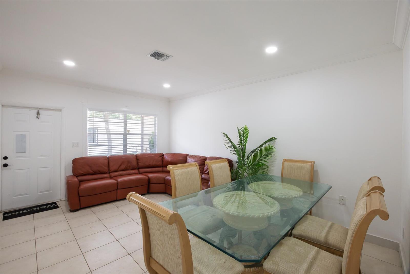 A dining area with a glass table and chairs sits beside a brown sectional sofa — 4591 Purdy Lane # 1, West Palm Beach FL 33415, WEST PALM BEACH, FL