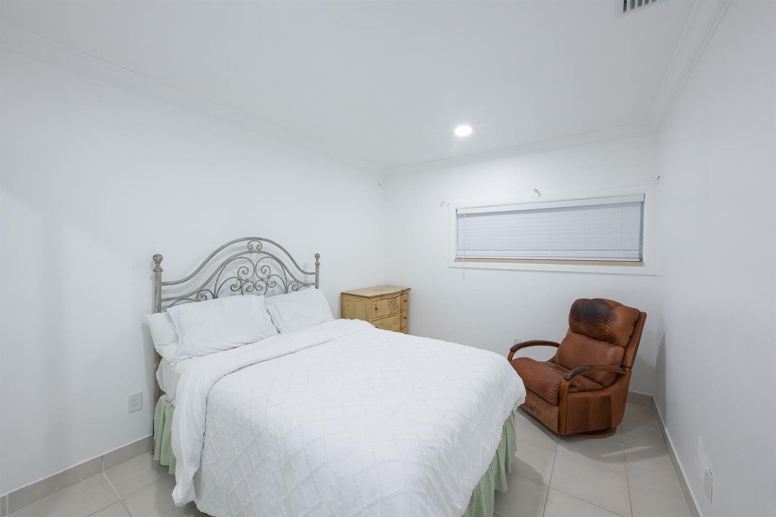 A bedroom features a white bed with a metal headboard, a wooden dresser, and a chair — 4591 Purdy Lane # 1, West Palm Beach FL 33415, WEST PALM BEACH, FL
