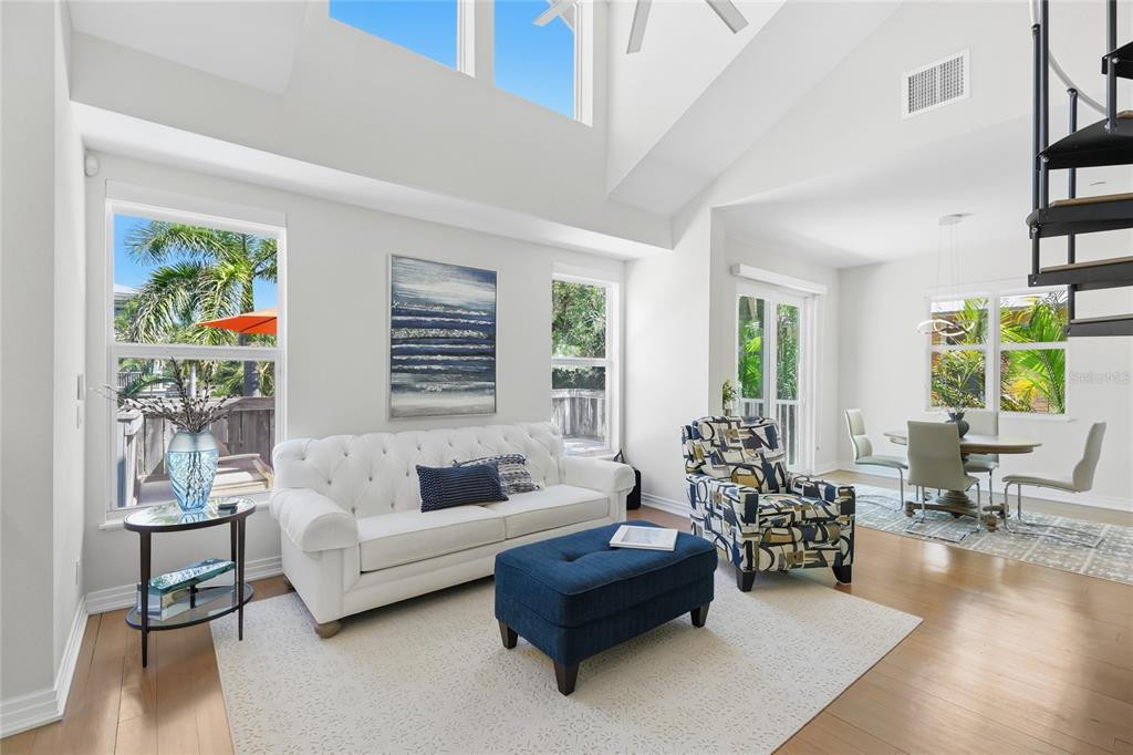 A bright living room features a white tufted sofa, blue ottoman, and a spiral staircase — 392 FIREHOUSE LANE, LONGBOAT KEY, FL