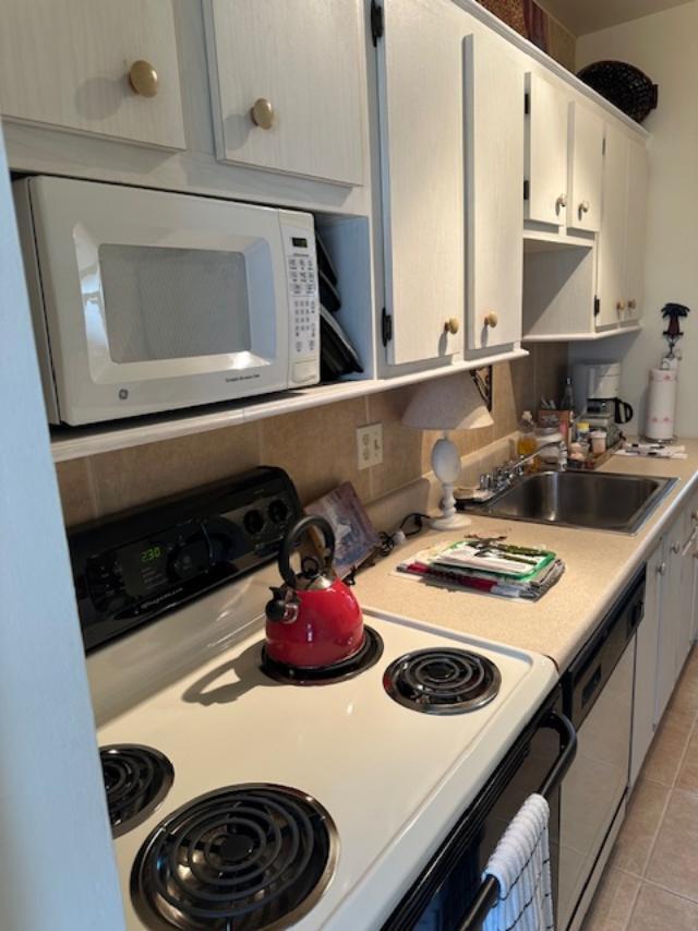 A kitchen features white cabinets, a microwave, a black electric stove, and a stainless sink — 550 NW 78th Avenue # 204, Margate FL 33063, MARGATE, FL
