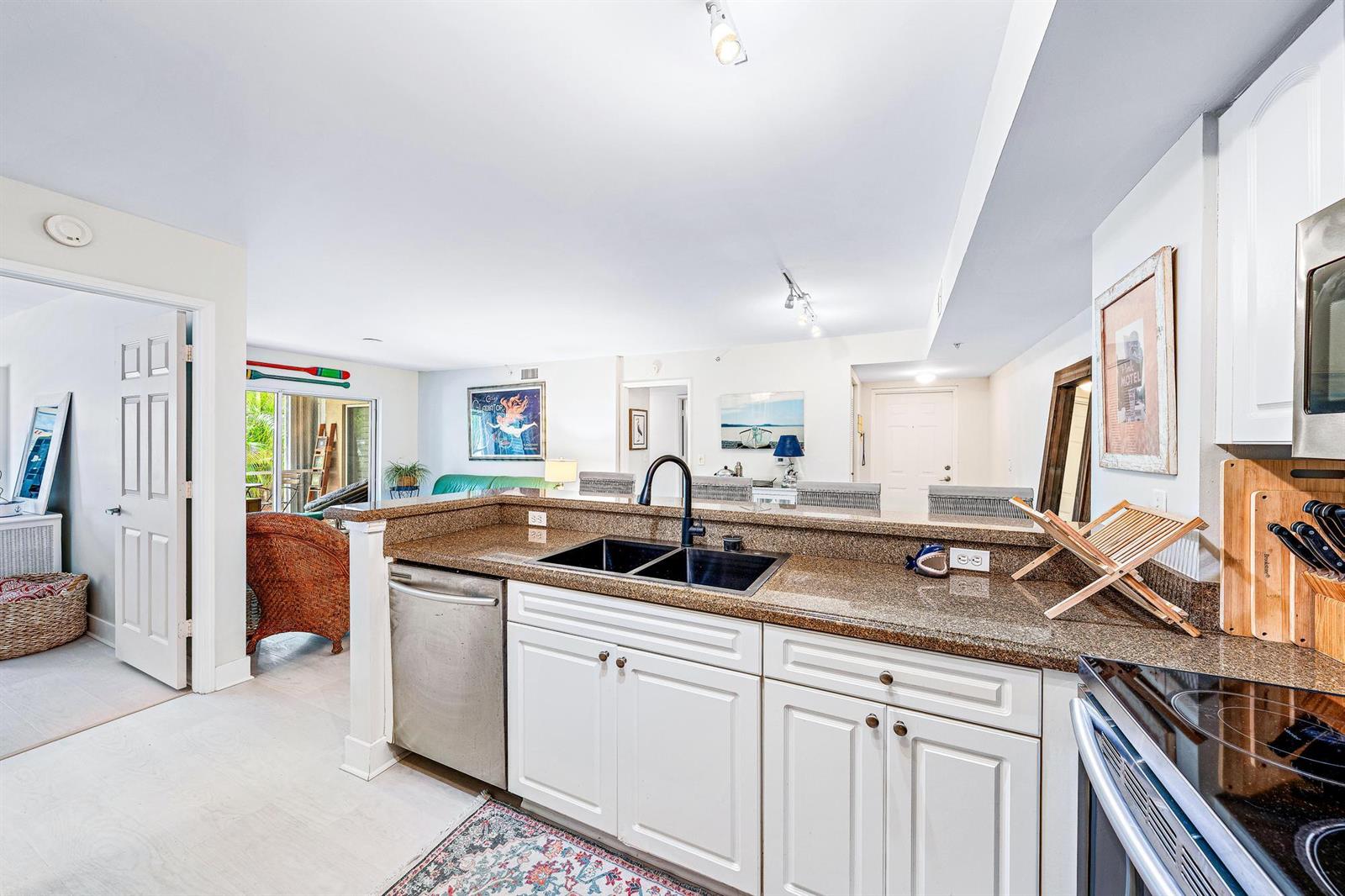 A kitchen with granite countertops, white cabinets, and a stainless steel dishwasher overlooks a living area — 242 Village Boulevard # 2109, Tequesta FL 33469, TEQUESTA, FL