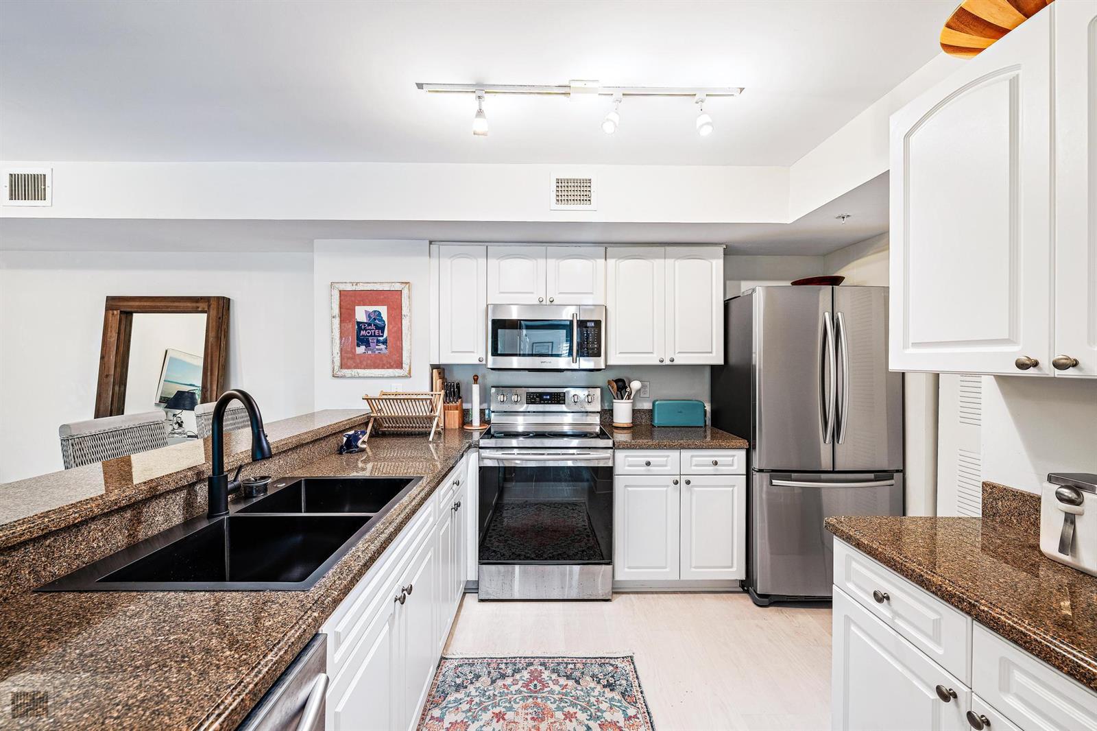 A kitchen features white cabinets, granite countertops, stainless steel appliances, and a black sink — 242 Village Boulevard # 2109, Tequesta FL 33469, TEQUESTA, FL