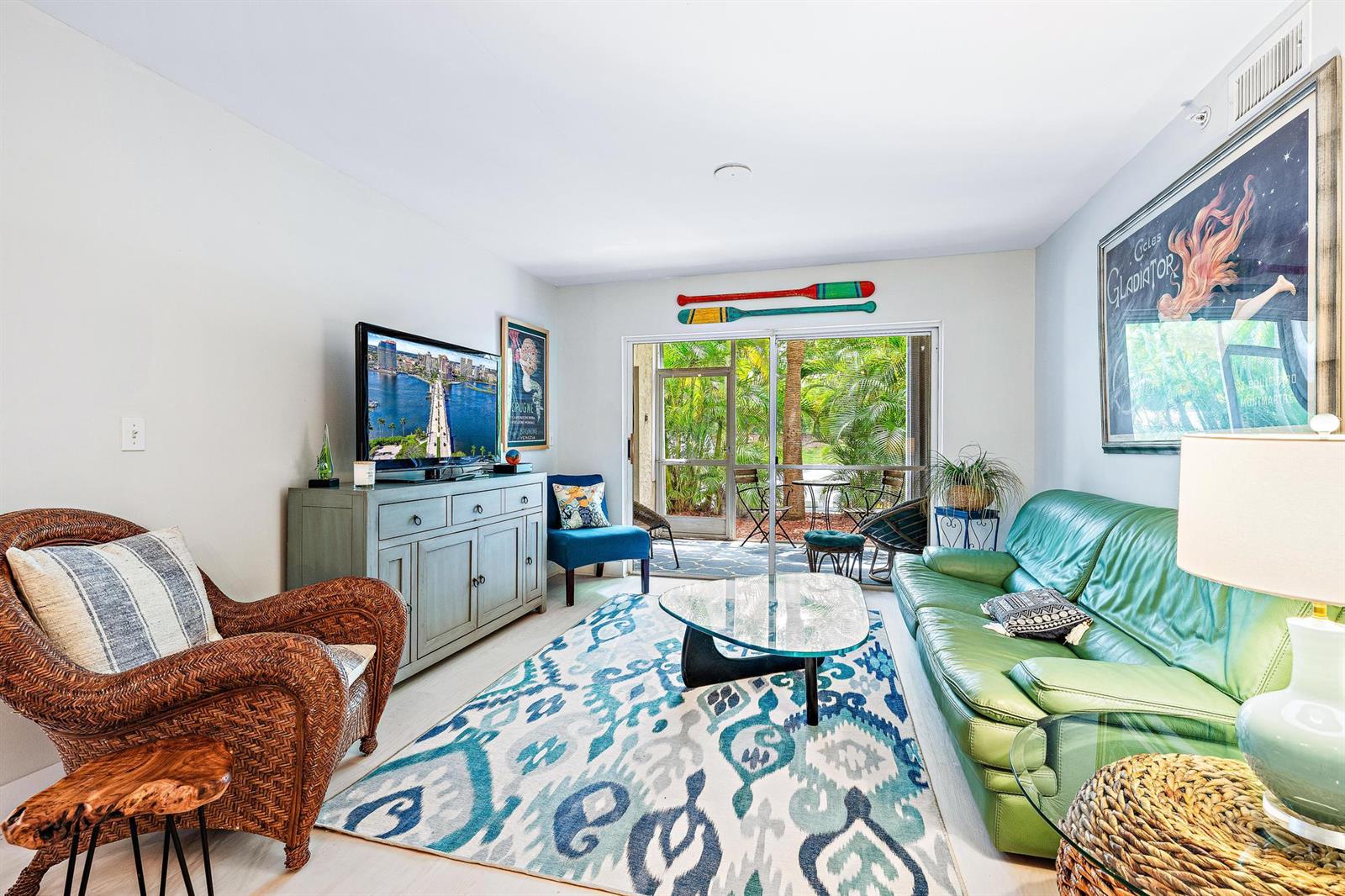 A living room features a green leather sofa, wicker chair, patterned rug, and sliding glass doors — 242 Village Boulevard # 2109, Tequesta FL 33469, TEQUESTA, FL