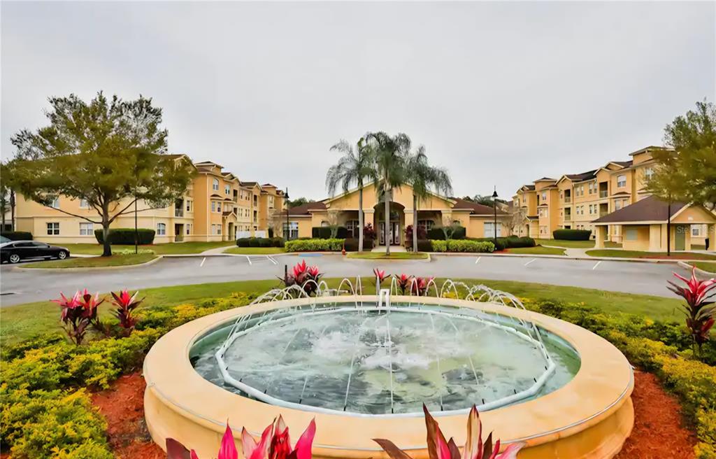 A circular fountain sits in the foreground of a multi-story apartment complex with palm trees — 818 TERRACE RIDGE CIRCLE UNIT 818, DAVENPORT, FL