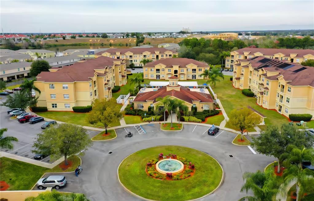 An aerial view shows a multi-story apartment complex with a central fountain and parking lot — 818 TERRACE RIDGE CIRCLE UNIT 818, DAVENPORT, FL
