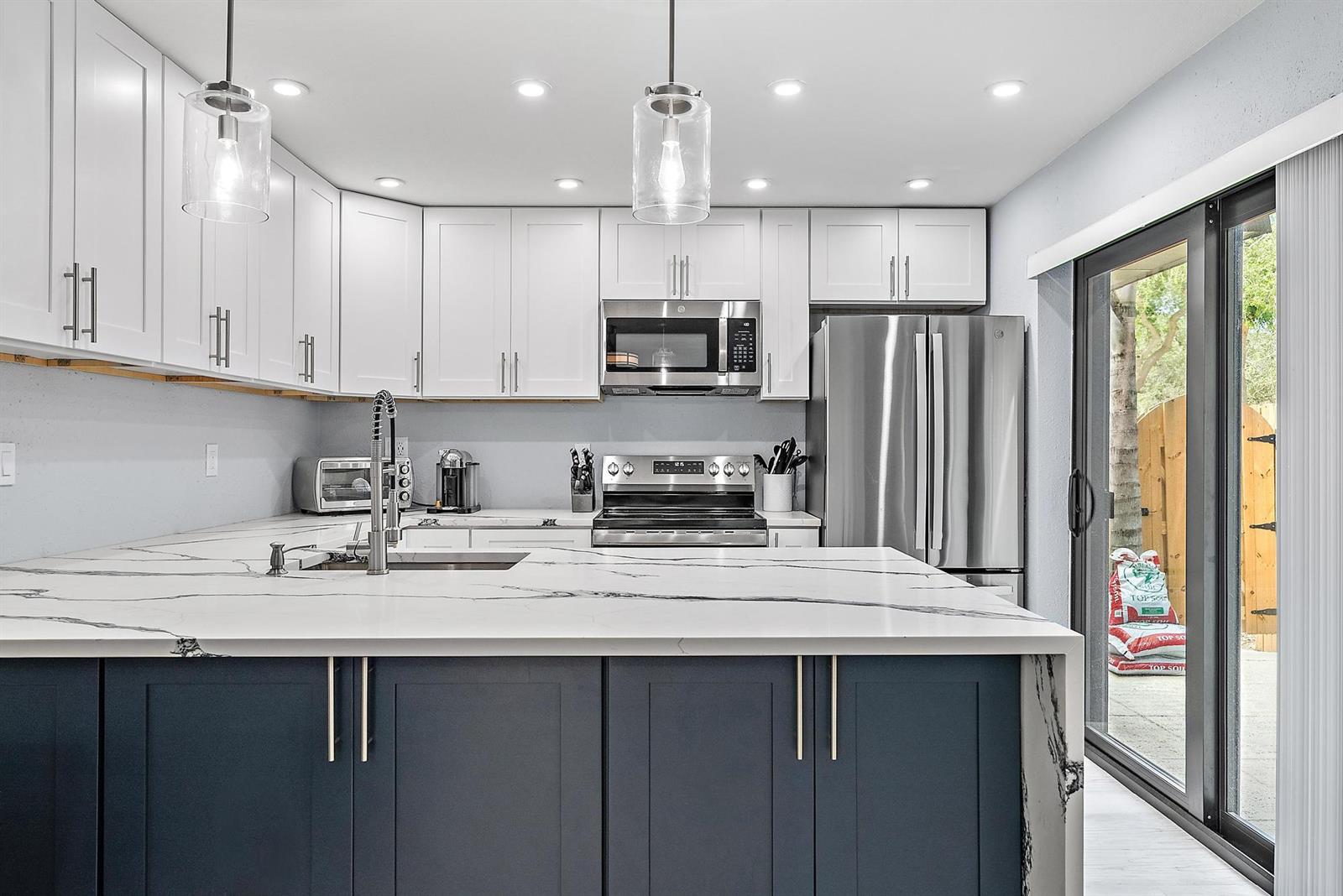 A kitchen features a large marble-topped island, dark blue cabinets, white upper cabinets, and stainless appliances — 2902 29th Court, Jupiter FL 33477, JUPITER, FL