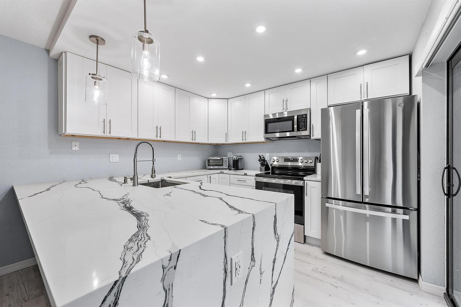 A kitchen features white cabinets, stainless steel appliances, and a large marble-patterned waterfall island — 2902 29th Court, Jupiter FL 33477, JUPITER, FL