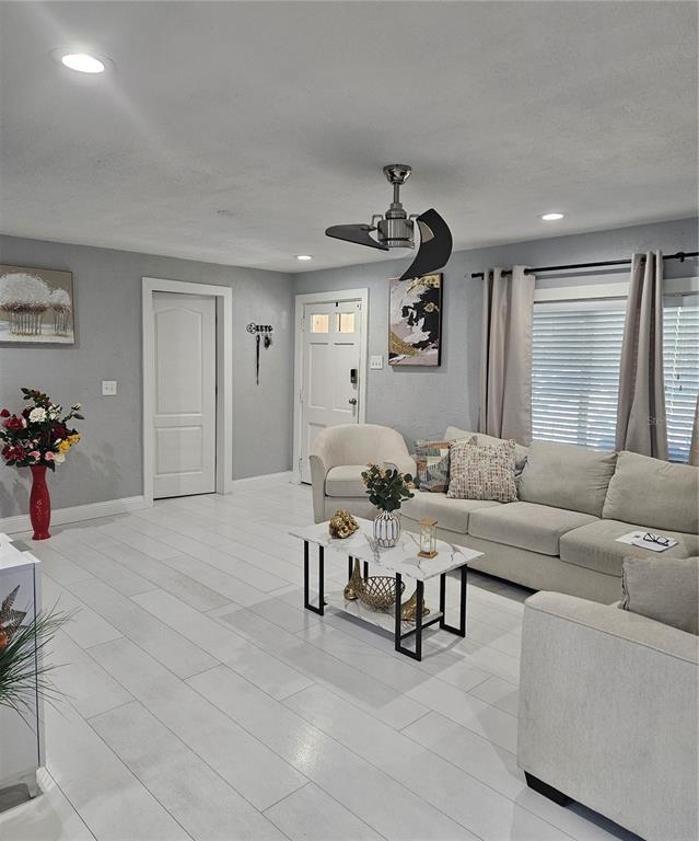 A living room features light gray walls, white tile flooring, a sectional sofa, and a ceiling fan — 9306 FOREST HILLS DRIVE, TAMPA, FL