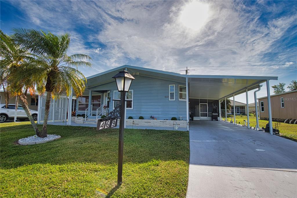 A light blue manufactured home features a front lawn, a palm tree, and a carport — 469 LOMA LINDA, NORTH PORT, FL