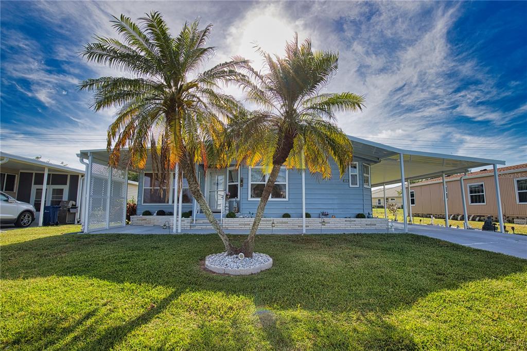 A light blue mobile home features a front palm tree, a carport, and a lawn — 469 LOMA LINDA, NORTH PORT, FL