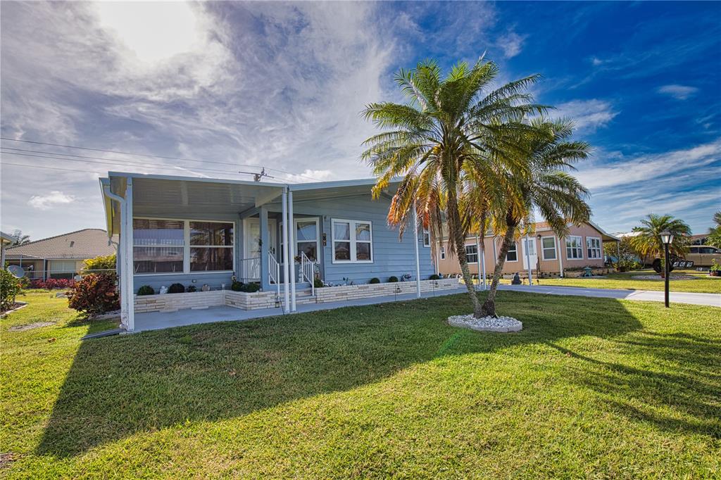 A light blue manufactured home features a covered porch, a palm tree, and a lawn — 469 LOMA LINDA, NORTH PORT, FL