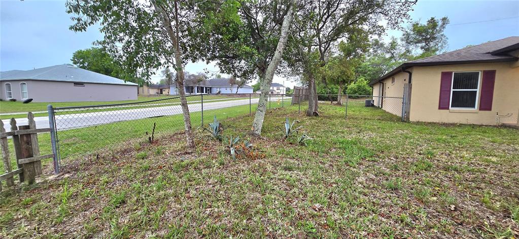 A grassy side yard features a chain-link fence, several trees, and a tan house exterior — 2729 SWEET SPRINGS STREET, DELTONA, FL