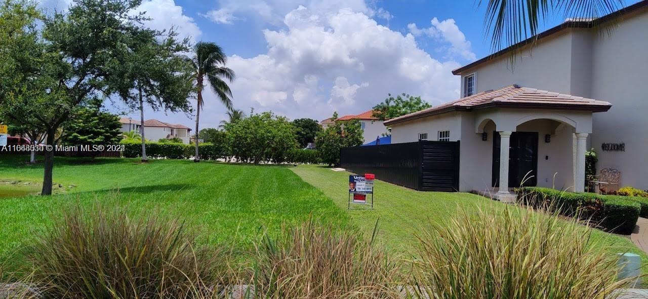 A grassy yard leads to the side entrance of a two-story house with a porch — 157th CT SW 65th TERRACE, Miami FL 33193, MIAMI, FL