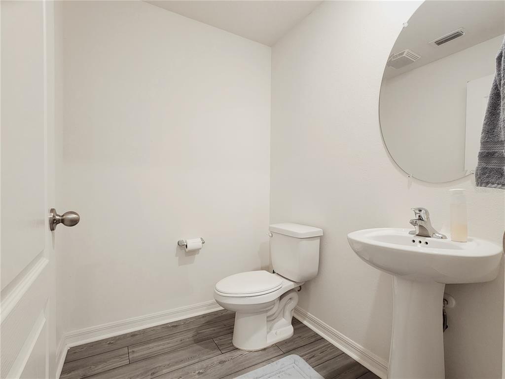 A half bathroom features a pedestal sink, a toilet, and grey wood-look flooring — 1679 WYNFORD CIRCLE, TAVARES, FL