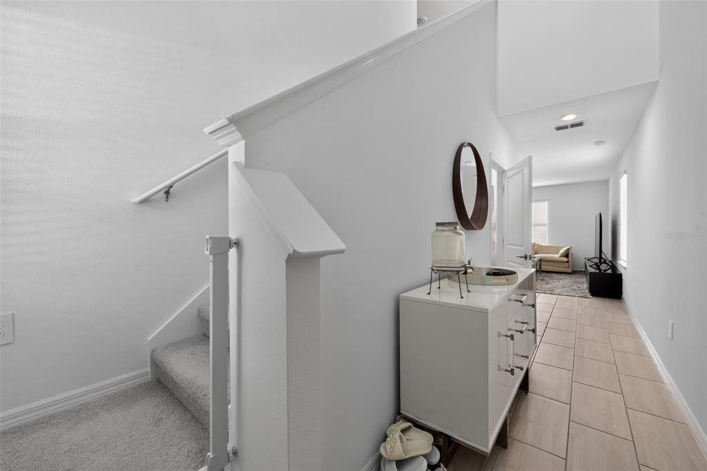A white hallway features a staircase with a baby gate, a console table, and tile flooring — 13065 EMPRESS JEWEL TRAIL, PARRISH, FL