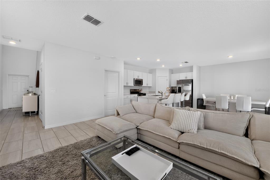 An open-concept living room features a large beige sectional sofa, tile flooring, and a kitchen — 13065 EMPRESS JEWEL TRAIL, PARRISH, FL