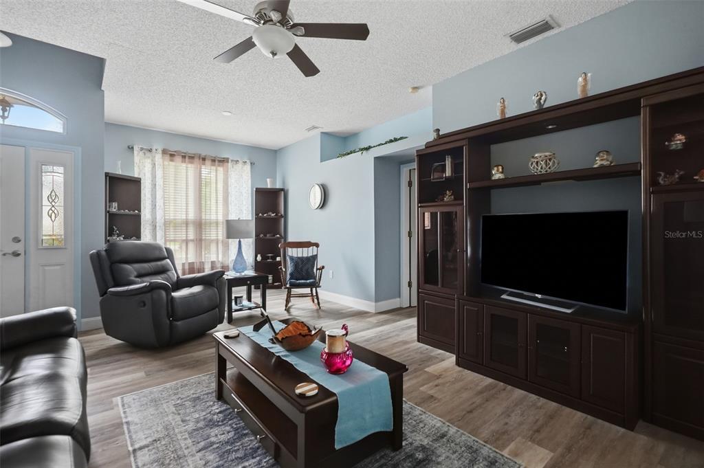 A living room features light blue walls, wood-look flooring, a ceiling fan, and dark wood furniture — 1087 TRINIDAD AVENUE, SPRING HILL, FL