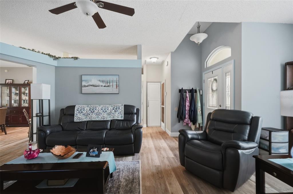 A living room with light gray walls, wood-look flooring, a black leather sofa, and armchair — 1087 TRINIDAD AVENUE, SPRING HILL, FL