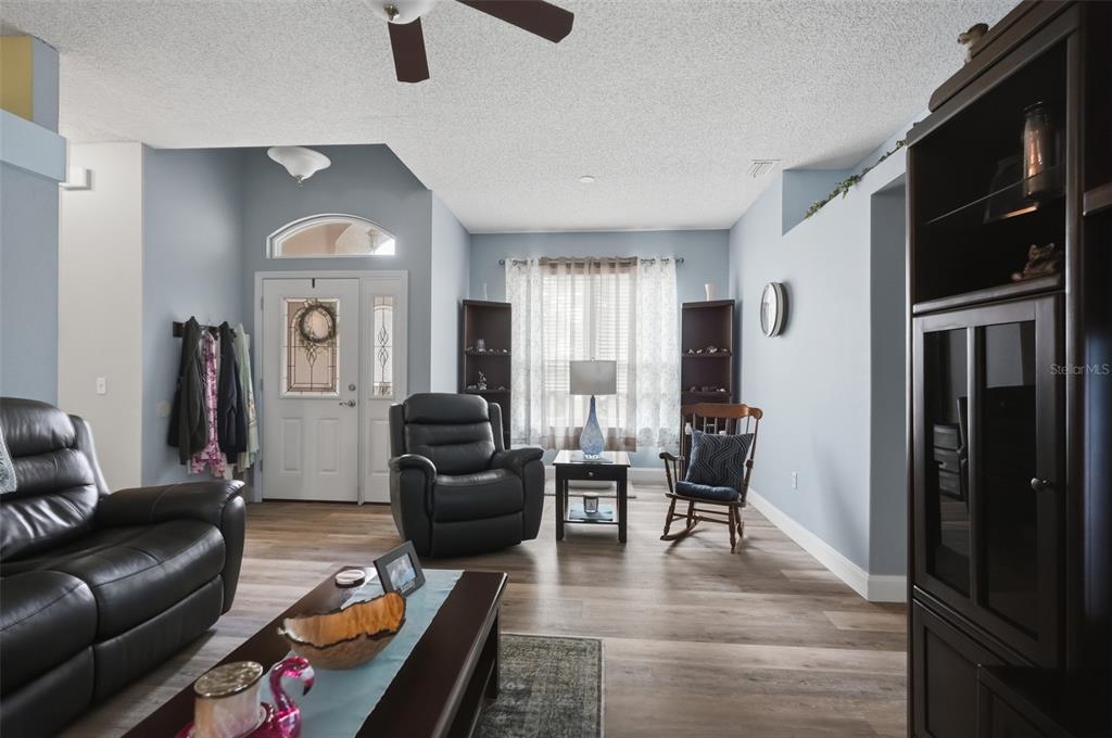 A living room features light blue walls, wood-look flooring, a ceiling fan, and dark furniture — 1087 TRINIDAD AVENUE, SPRING HILL, FL