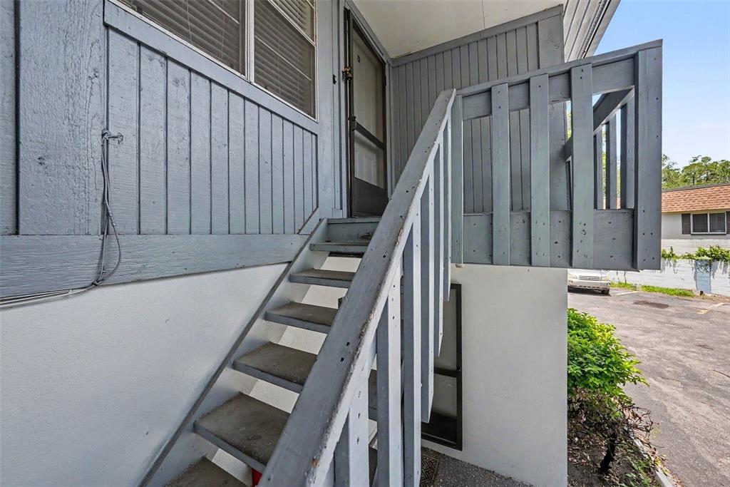 An exterior view shows a set of wooden stairs leading to an elevated building entrance — 9208 N CONNECHUSETT ROAD UNIT D, TAMPA, FL