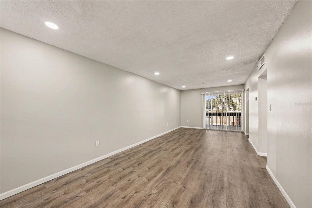 An empty living room features light gray walls, wood-look flooring, recessed lighting, and a sliding door — 9208 N CONNECHUSETT ROAD UNIT D, TAMPA, FL