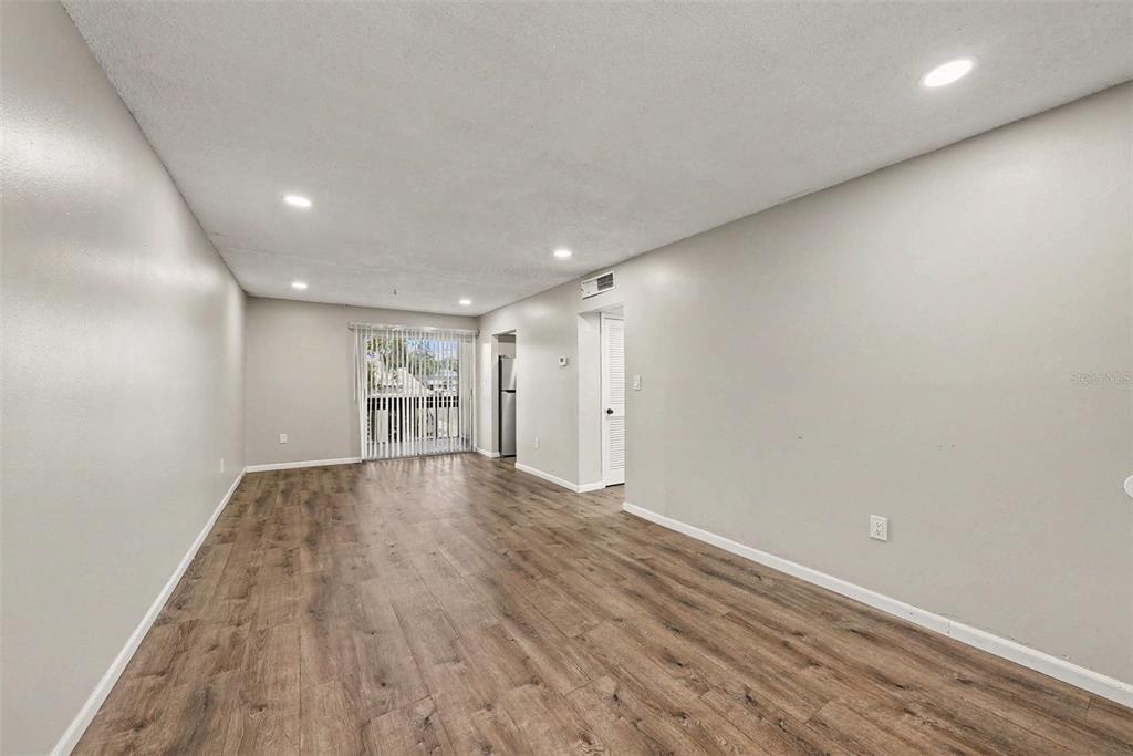 An empty room with light gray walls, wood-look flooring, recessed lighting, and a sliding glass door — 9208 N CONNECHUSETT ROAD UNIT D, TAMPA, FL