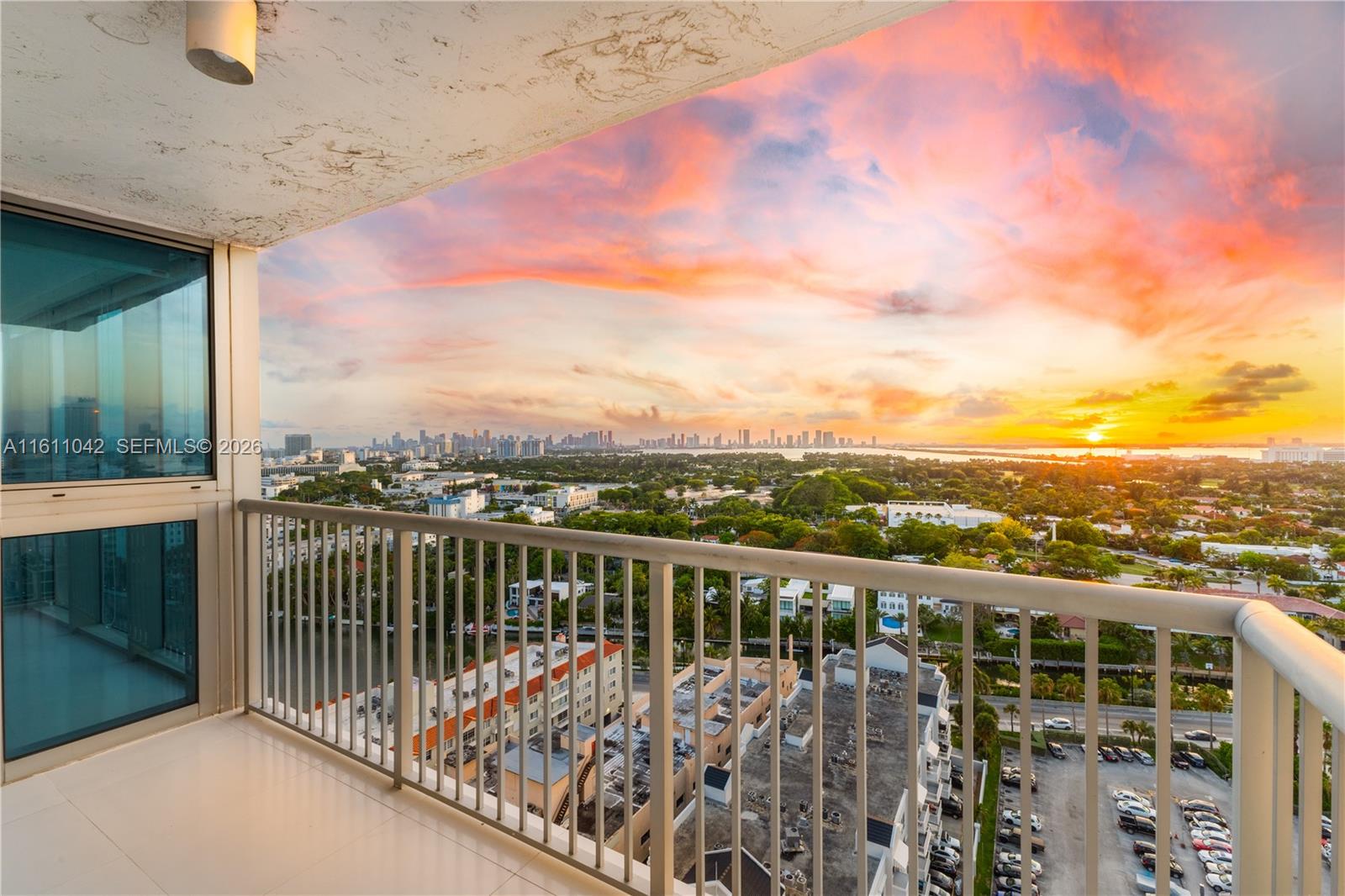 A high-rise balcony overlooks a suburban landscape and city skyline during a vibrant sunset — 2655 Collins Ave # 2302, Miami Beach FL 33140, MIAMI BEACH, FL