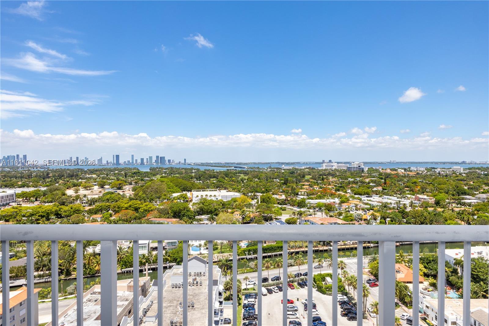 A high-angle view from a balcony overlooks a suburban landscape, a waterway, and a distant skyline — 2655 Collins Ave # 2302, Miami Beach FL 33140, MIAMI BEACH, FL