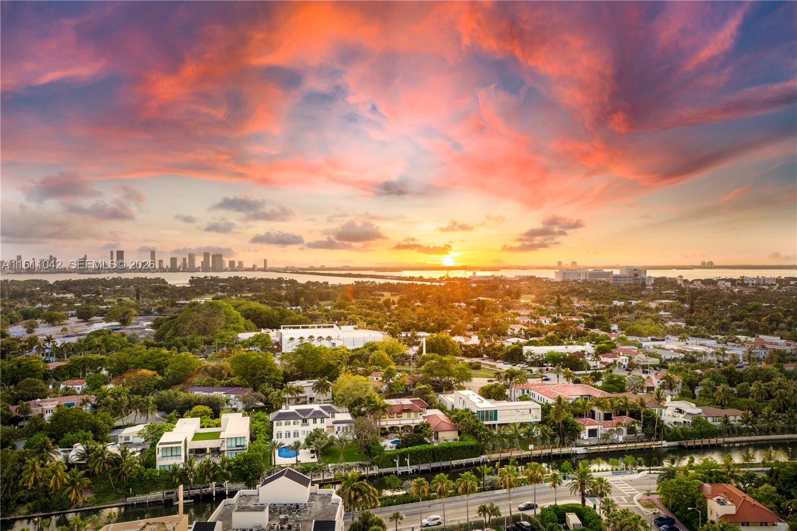An aerial view shows a residential neighborhood with lush trees, canals, and a sunset sky — 2655 Collins Ave # 2302, Miami Beach FL 33140, MIAMI BEACH, FL