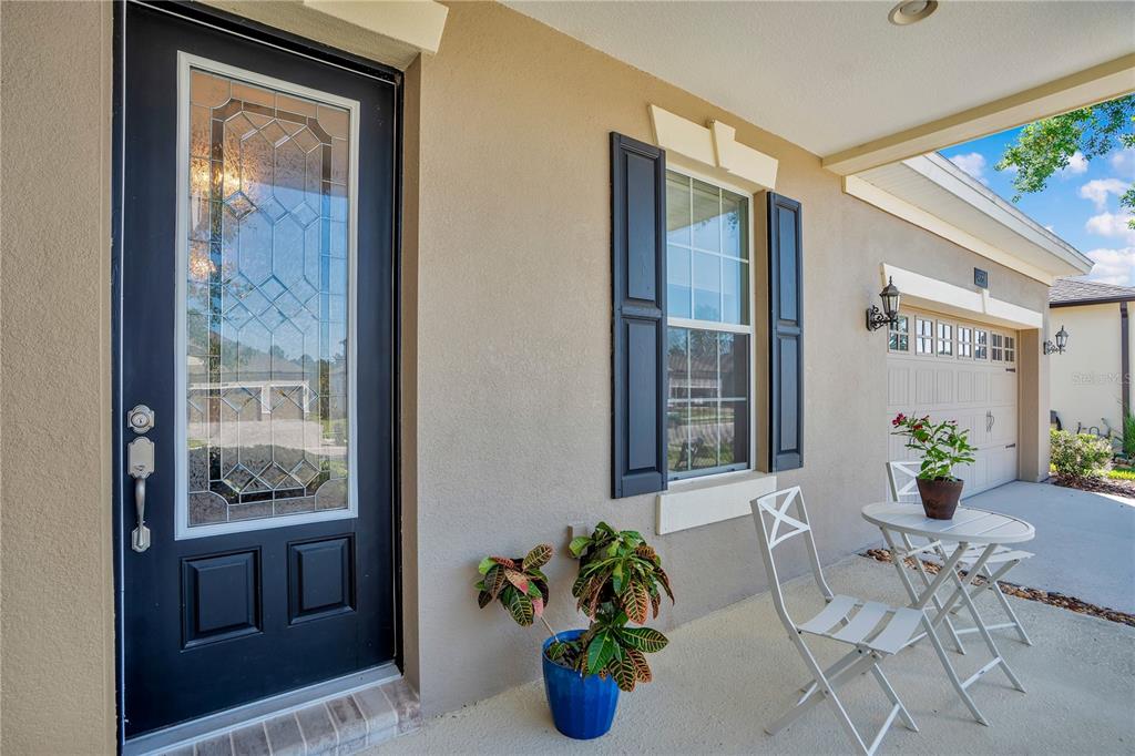 A front porch features a black door with glass panels, a window with shutters, and furniture — 4684 SOUTHERN VALLEY LOOP, BROOKSVILLE, FL