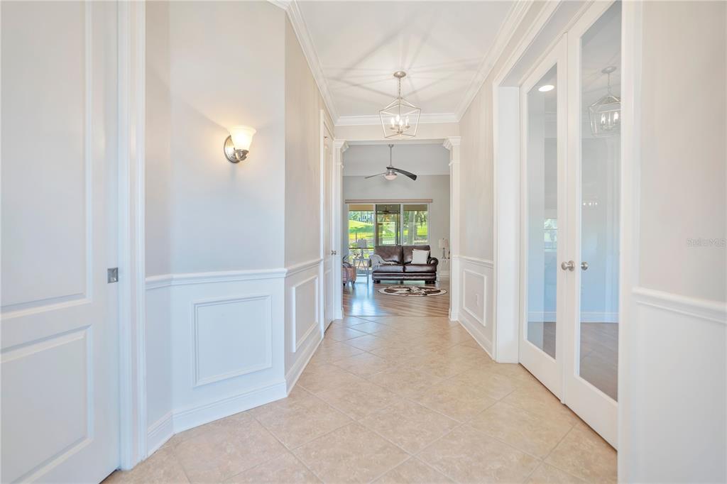 A tiled hallway with wainscoting leads to a living room with a leather sofa — 4684 SOUTHERN VALLEY LOOP, BROOKSVILLE, FL