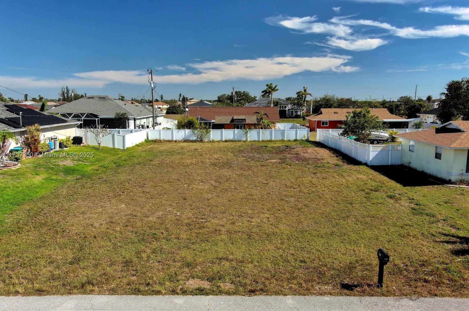 An elevated view of a vacant, grassy residential lot enclosed by white vinyl fencing — 2013 NE 18th Ave, Cape Coral FL 33909, CAPE CORAL, FL