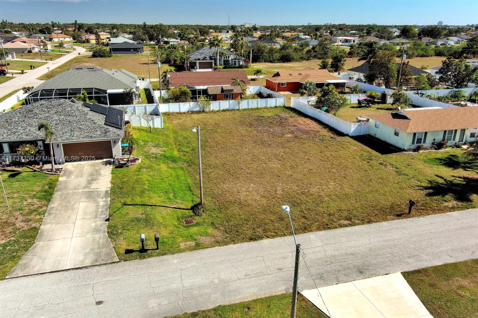 An aerial view shows a vacant residential lot situated between two houses with white fences — 2013 NE 18th Ave, Cape Coral FL 33909, CAPE CORAL, FL