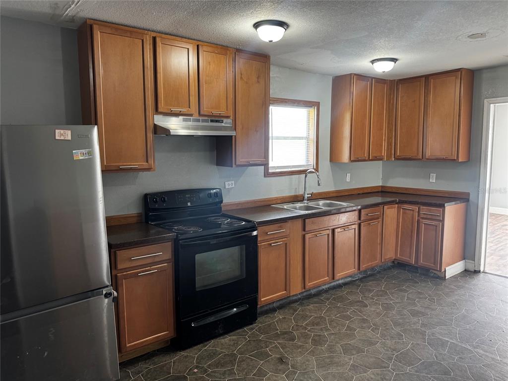 A kitchen with wood cabinets, dark countertops, stainless steel appliances, and gray tile flooring — 7001 COLUMBIA DRIVE, MULBERRY, FL