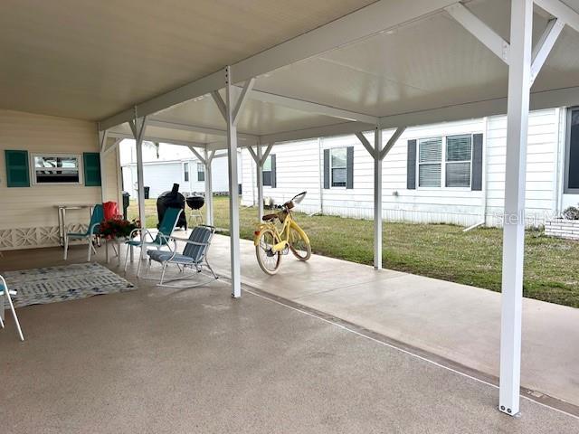 A covered concrete carport features a yellow bicycle, outdoor chairs, and a grill — 347 MARINER DRIVE, NORTH PORT, FL
