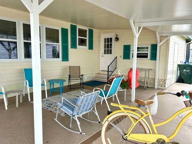 A covered patio features outdoor furniture, a yellow bicycle, and teal shutters on a light-colored home — 347 MARINER DRIVE, NORTH PORT, FL