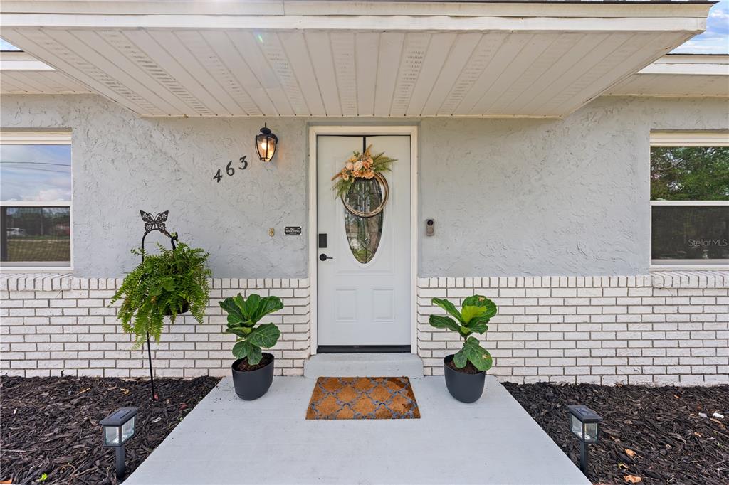 A white front door with a wreath is centered between two potted plants and windows — 463 CHESTNUT COURT, DELTONA, FL