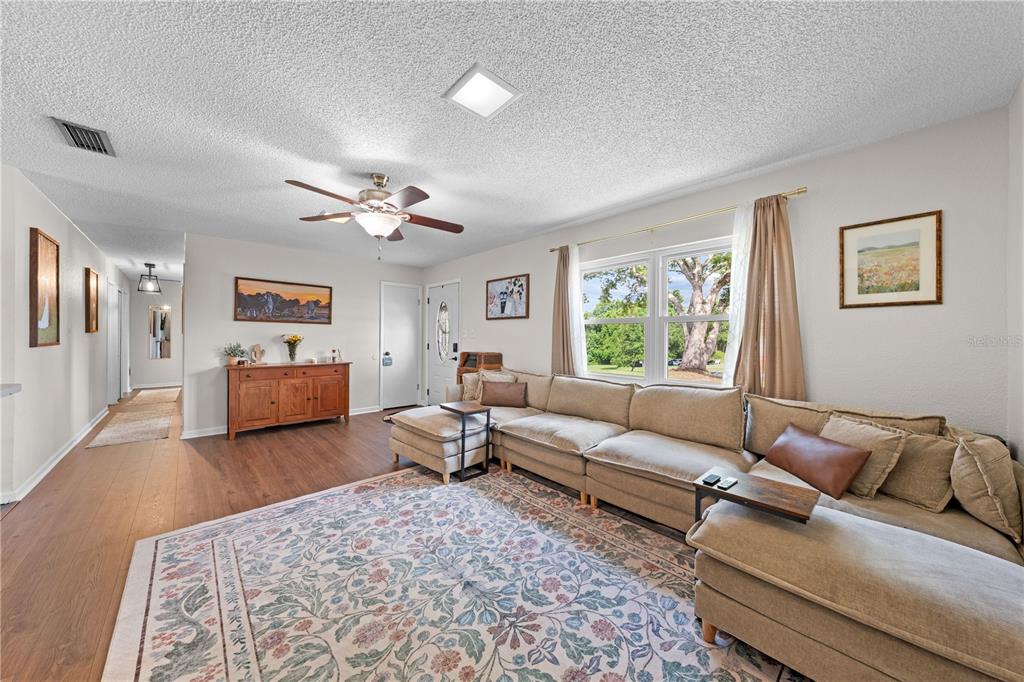 A living room features a large sectional sofa, a floral area rug, and wood flooring — 463 CHESTNUT COURT, DELTONA, FL