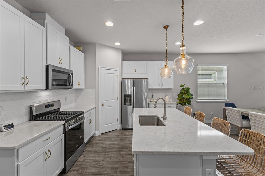 A modern kitchen features white cabinetry, a large quartz island, stainless steel appliances, and wood-look flooring — 5429 HOPE SOUND CIRCLE, SARASOTA, FL