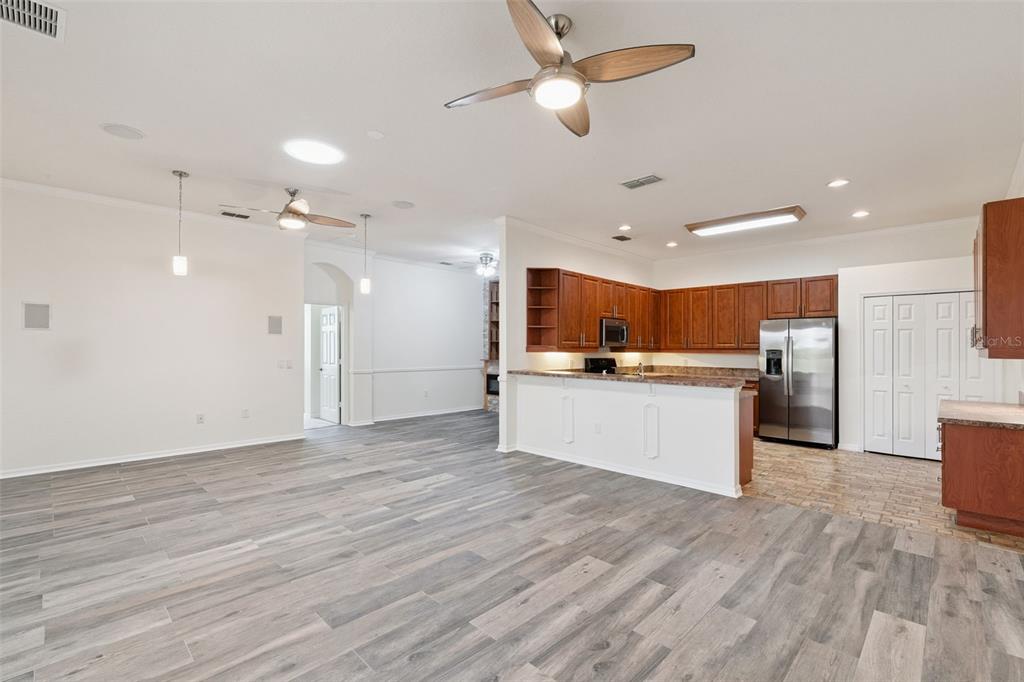A spacious open-concept kitchen and living area features wood-look tile flooring and wooden cabinets — 813 SUMMIT GREENS BOULEVARD, CLERMONT, FL