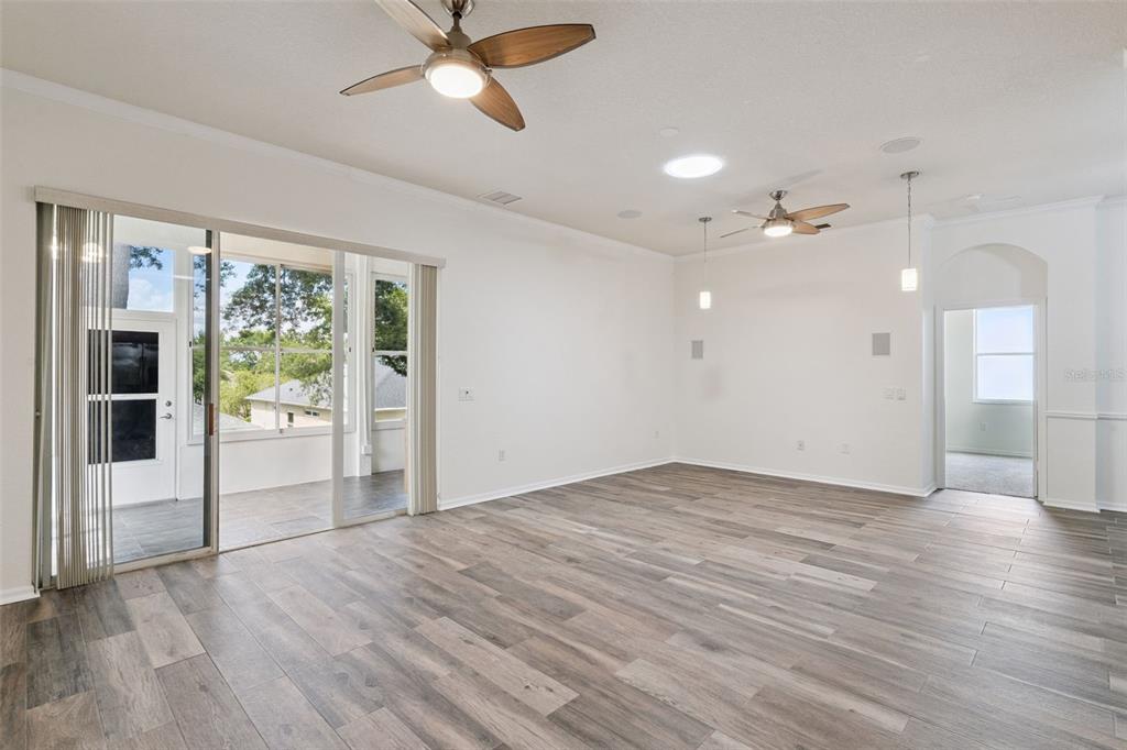 An empty living room features wood-look tile flooring, two ceiling fans, and sliding glass doors — 813 SUMMIT GREENS BOULEVARD, CLERMONT, FL