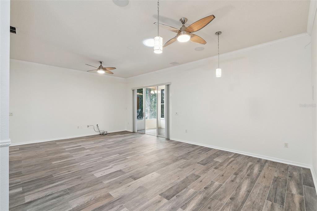 A spacious living room features wood-look tile flooring, two ceiling fans, and sliding glass doors — 813 SUMMIT GREENS BOULEVARD, CLERMONT, FL
