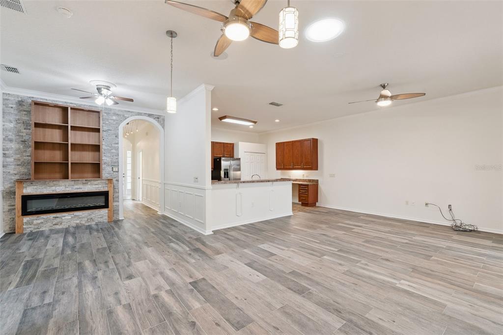 An open-concept living and kitchen area features wood-look flooring, a stone fireplace, and ceiling fans — 813 SUMMIT GREENS BOULEVARD, CLERMONT, FL