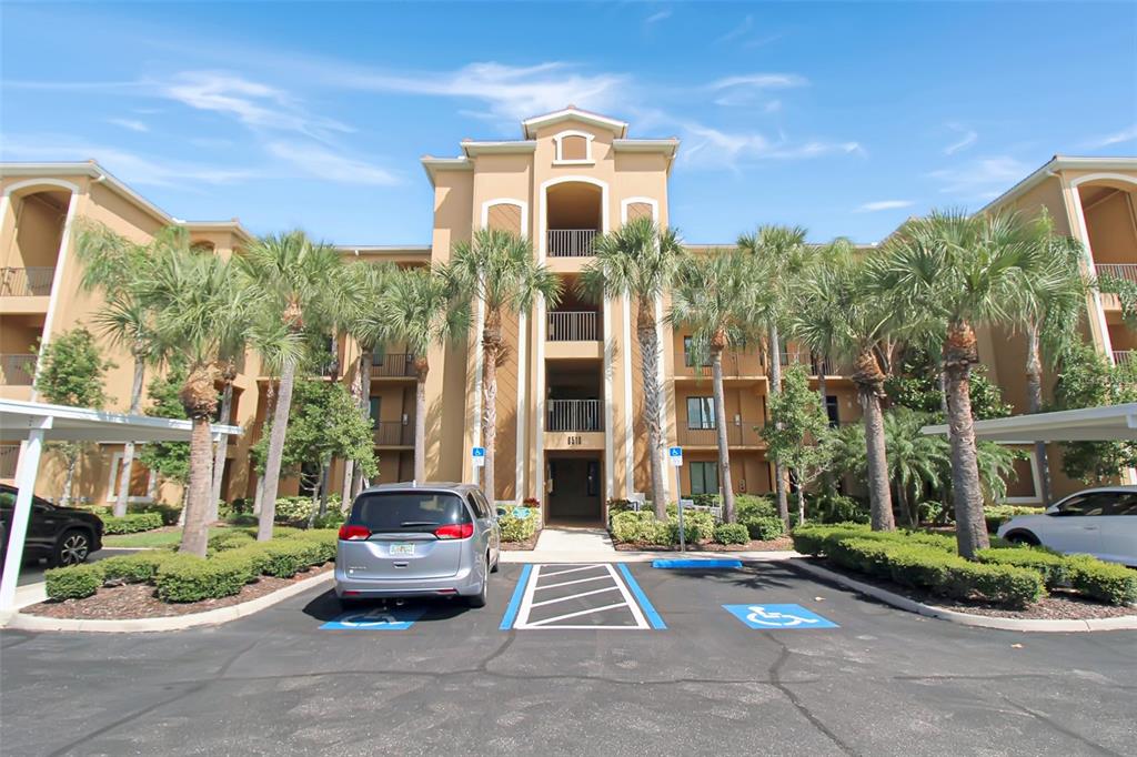 A multi-story tan apartment building with palm trees and a handicap-accessible parking lot in front — 6519 GRAND ESTUARY TRAIL UNIT 302, BRADENTON, FL