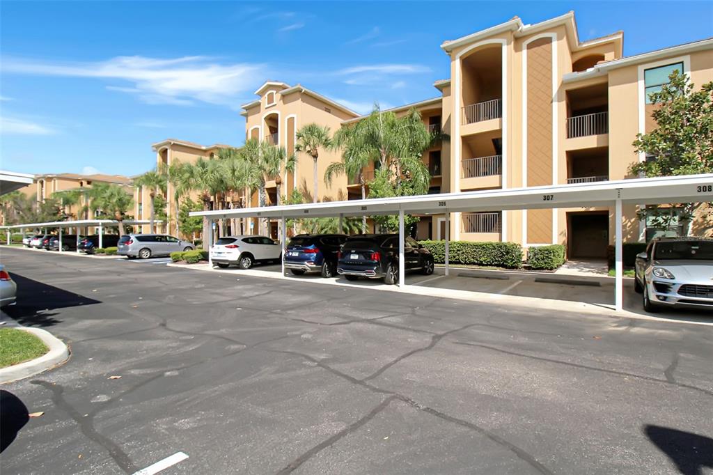 An exterior view of a multi-story apartment building with covered parking spaces in front — 6519 GRAND ESTUARY TRAIL UNIT 302, BRADENTON, FL